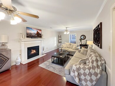 Living room with ornamental molding, a ceiling fan, dark wood finished floors, and a fireplace with flush hearth