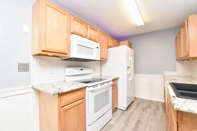 Kitchen featuring wainscoting, backsplash, white appliances, light brown cabinetry, and light wood-type flooring