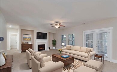 Living room with light colored carpet, a lit fireplace, ceiling fan, and french doors