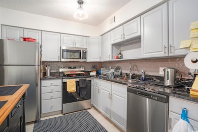 Kitchen with appliances with stainless steel finishes, a textured ceiling, white cabinetry, and light tile patterned floors