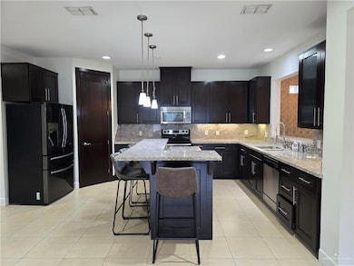 Kitchen with stainless steel appliances, decorative backsplash, a kitchen bar, light stone counters, and decorative light fixtures