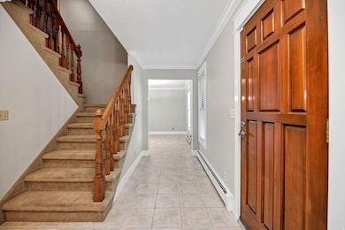 Entryway featuring a baseboard heating unit, ornamental molding, stairs, and light tile patterned floors