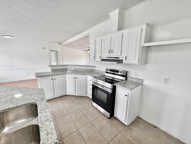 Kitchen with stainless steel electric stove, under cabinet range hood, a peninsula, a sink, and white cabinets