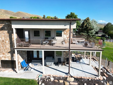 Rear view of property featuring a balcony, stone siding, a mountain view, and a patio