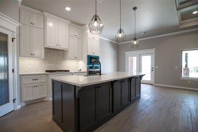 Kitchen featuring hanging light fixtures, black microwave, crown molding, and a kitchen island with sink