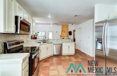 Kitchen with appliances with stainless steel finishes, light countertops, white cabinets, a peninsula, and decorative backsplash