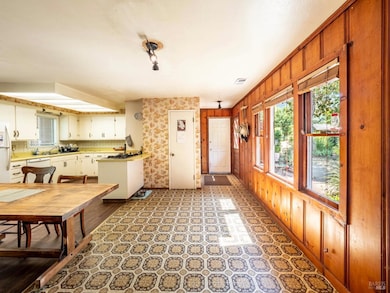 Adjoining the kitchen, the dining area sits at the edge of the sunlit hallway which is wrapped in knotty pine paneling. The large windows provide views of the gardens.