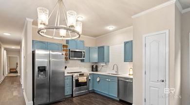 Kitchen with blue cabinetry, appliances with stainless steel finishes, backsplash, crown molding, and hanging light fixtures