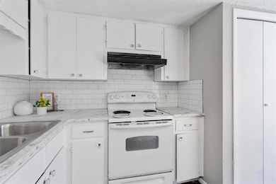 Kitchen featuring white range with electric cooktop, light countertops, white cabinetry, under cabinet range hood, and tasteful backsplash