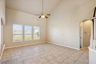 Spacious living room with high ceilings, natural light from three large windows, tiled flooring, and a ceiling fan. The room features an arched entryway, neutral walls, and easy access to other areas of the home.