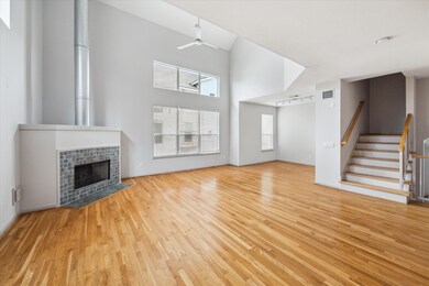 This spacious living area features high ceilings, a modern fireplace, and large windows for natural light. The open layout flows into a staircase, enhancing the airy feel, while the hardwood floors add warmth and elegance.