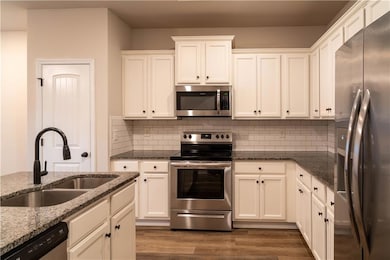 Kitchen with appliances with stainless steel finishes, decorative backsplash, dark wood-style floors, and white cabinets
