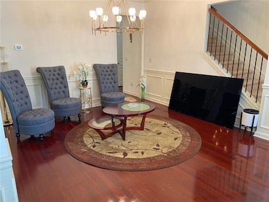 Sitting room with wood finished floors, a decorative wall, a chandelier, stairway, and wainscoting