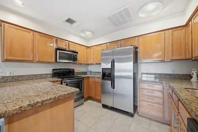 Kitchen with appliances with stainless steel finishes, light stone countertops, light tile patterned flooring, and brown cabinets