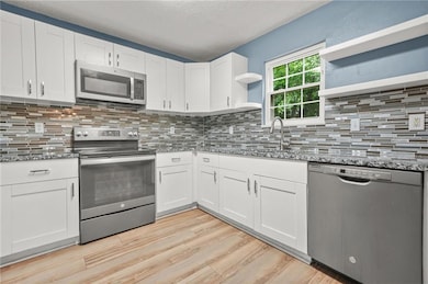 Kitchen featuring stainless steel appliances, open shelves, stone counters, light wood finished floors, and white cabinetry