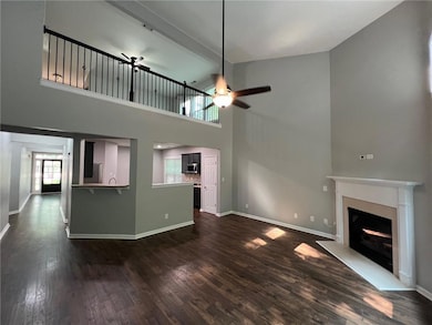 Unfurnished living room featuring a fireplace with raised hearth, ceiling fan, dark wood-type flooring, high vaulted ceiling, and baseboards