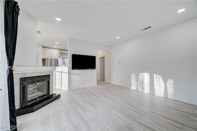 Unfurnished living room featuring recessed lighting, arched walkways, light wood finished floors, and a tiled fireplace