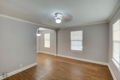 Empty room featuring ornamental molding, dark wood finished floors, arched walkways, and ceiling fan