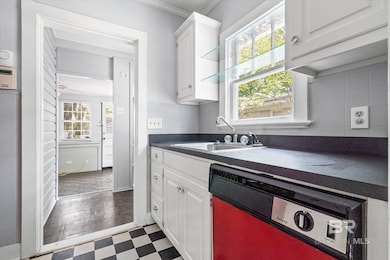 Kitchen featuring dishwashing machine, white cabinets, dark countertops, dark flooring, and decorative backsplash