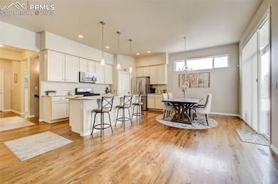 Kitchen with light wood-type flooring, decorative backsplash, a kitchen breakfast bar, and stainless steel appliances