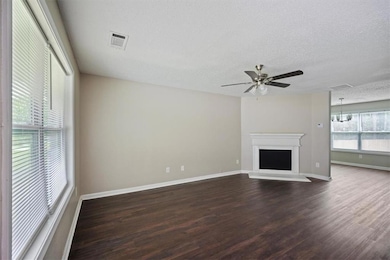 Unfurnished living room featuring dark wood finished floors, a textured ceiling, ceiling fan, baseboards, and a fireplace with raised hearth
