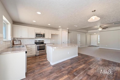 Kitchen featuring appliances with stainless steel finishes, a kitchen island, backsplash, healthy amount of natural light, and a textured ceiling