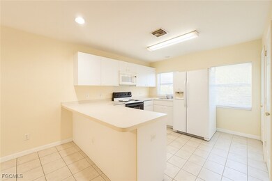 Kitchen with light countertops, a peninsula, white appliances, light tile patterned floors, and white cabinets