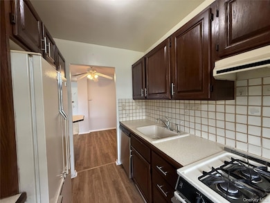 Kitchen featuring gas range, freestanding refrigerator, tasteful backsplash, dark brown cabinetry, and light countertops