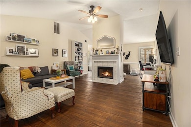 Living room with lofted ceiling, dark wood-style floors, a tiled fireplace, and ceiling fan