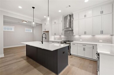 Kitchen with wall chimney range hood, stainless steel gas stove, a sink, tasteful backsplash, and light wood-style floors
