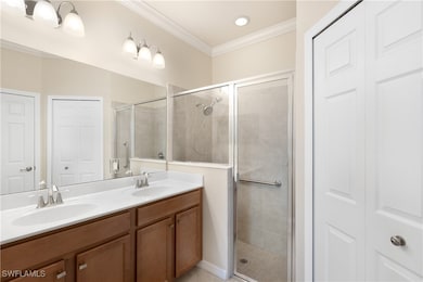 Primary Bathroom featuring a closet, a shower stall, crown molding, double vanity, and light tile patterned floors