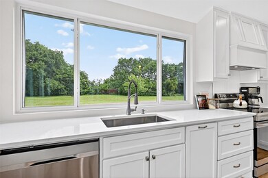 Kitchen with stainless steel appliances, white cabinetry, light countertops, and custom range hood