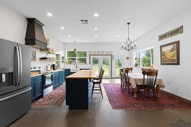 Kitchen with appliances with stainless steel finishes, butcher block counters, finished concrete flooring, blue cabinetry, and wall chimney exhaust hood