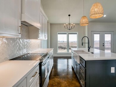 Kitchen featuring hanging light fixtures, electric range, tasteful backsplash, an island with sink, and white cabinetry