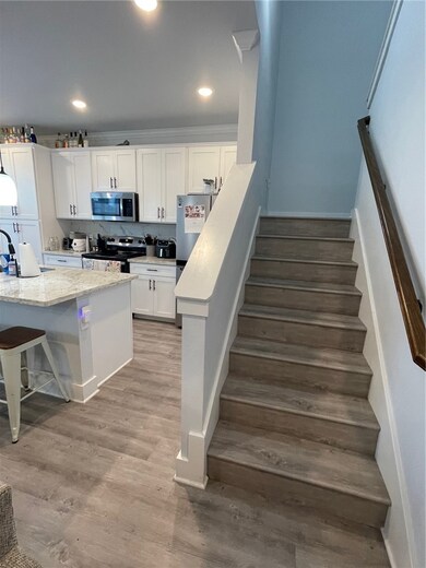 Kitchen with a breakfast bar, white cabinetry, stove, light wood-style floors, and stainless steel refrigerator