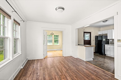 Unfurnished living room featuring crown molding, dark wood finished floors, and a baseboard heating unit