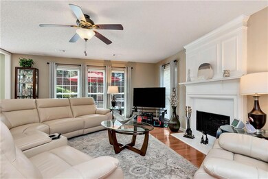 Living area with a ceiling fan, wood finished floors, a fireplace with raised hearth, and a textured ceiling