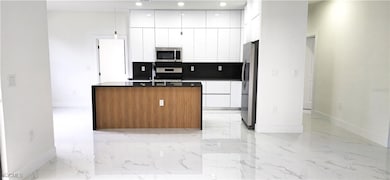 Kitchen with an island with sink, stainless steel appliances, pendant lighting, white cabinetry, and dark stone countertops