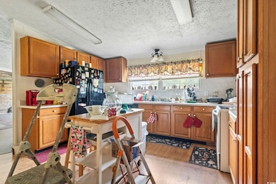 Kitchen featuring range, light wood finished floors, a textured ceiling, brown cabinets, and light countertops