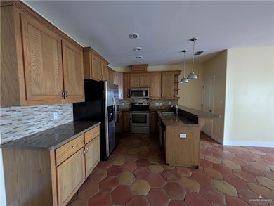 Kitchen featuring appliances with stainless steel finishes, a sink, a peninsula, open shelves, and tasteful backsplash