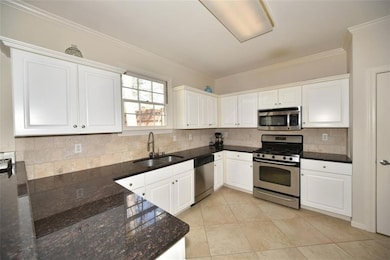 Kitchen with stainless steel appliances, decorative backsplash, white cabinets, dark stone countertops, and light tile patterned flooring