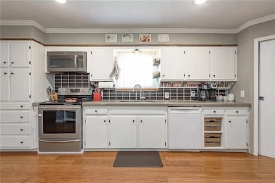 Kitchen with appliances with stainless steel finishes, decorative backsplash, white cabinets, crown molding, and light wood-style flooring