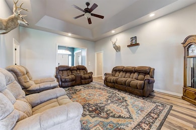 Living area featuring a tray ceiling, ceiling fan, wood finished floors, recessed lighting, and baseboards