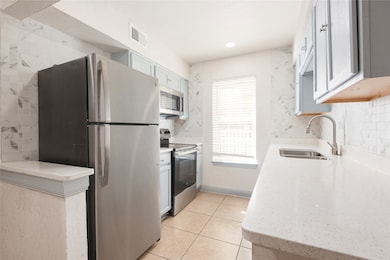 Kitchen featuring appliances with stainless steel finishes, light stone counters, light tile patterned floors, white cabinets, and tasteful backsplash
