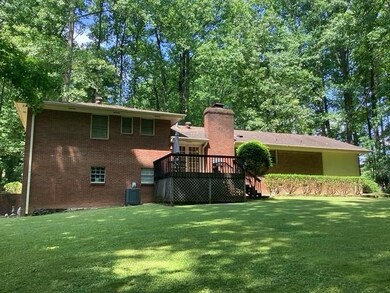 Back of house with a deck, a yard, a chimney, brick siding, and central AC