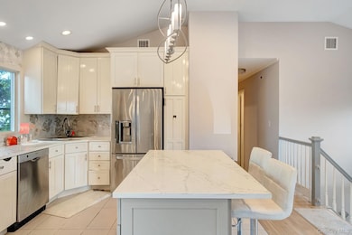 Kitchen with lofted ceiling, appliances with stainless steel finishes, pendant lighting, a kitchen breakfast bar, and backsplash