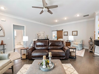 Living room with a ceiling fan, ornamental molding, dark wood-style floors, a barn door, and recessed lighting