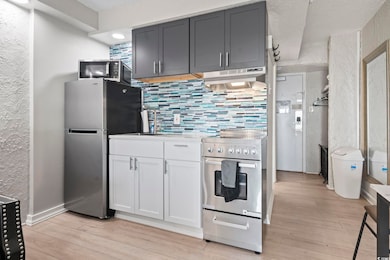 Kitchen featuring appliances with stainless steel finishes, under cabinet range hood, decorative backsplash, light wood-style floors, and a textured wall