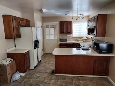 Kitchen featuring white appliances, under cabinet range hood, a peninsula, light countertops, and stone finish flooring