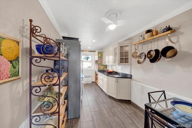 Kitchen with dark countertops, ornamental molding, wainscoting, wood finish floors, and glass insert cabinets
